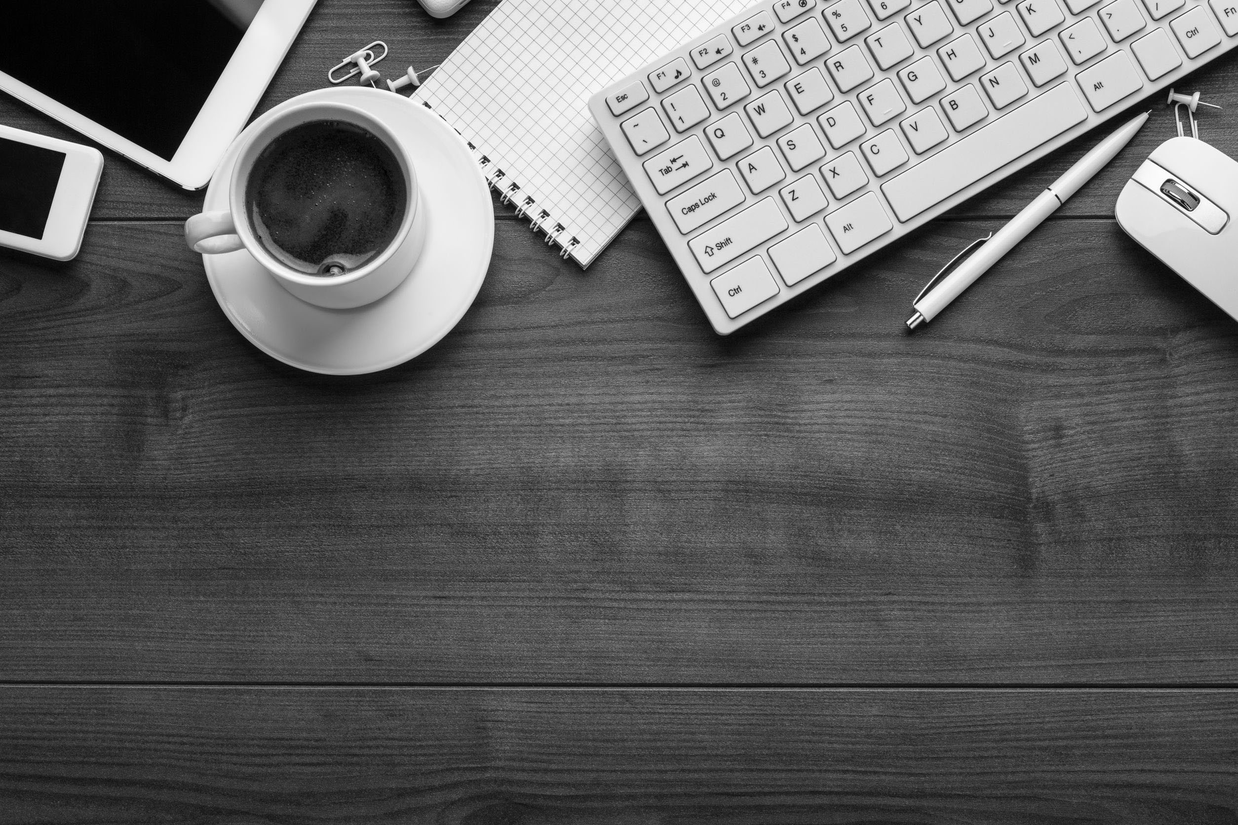 Grayscale photos of a wooden desk with coffee mug, notepad, tablet, and cellphone